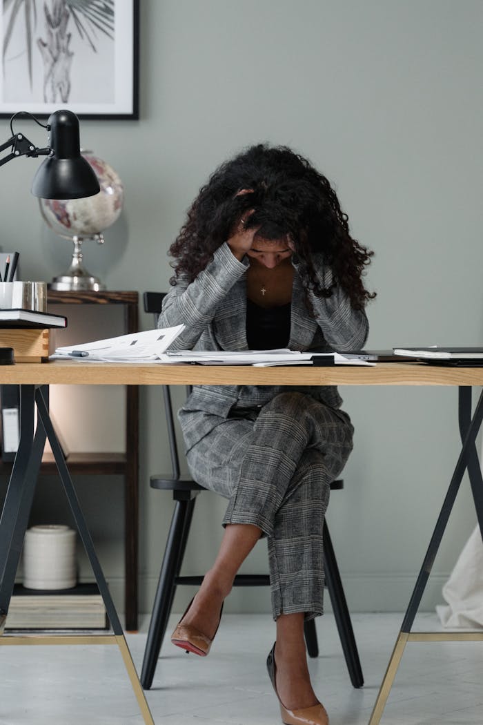 A frustrated businesswoman sitting at a desk, stressed in a modern office setting.